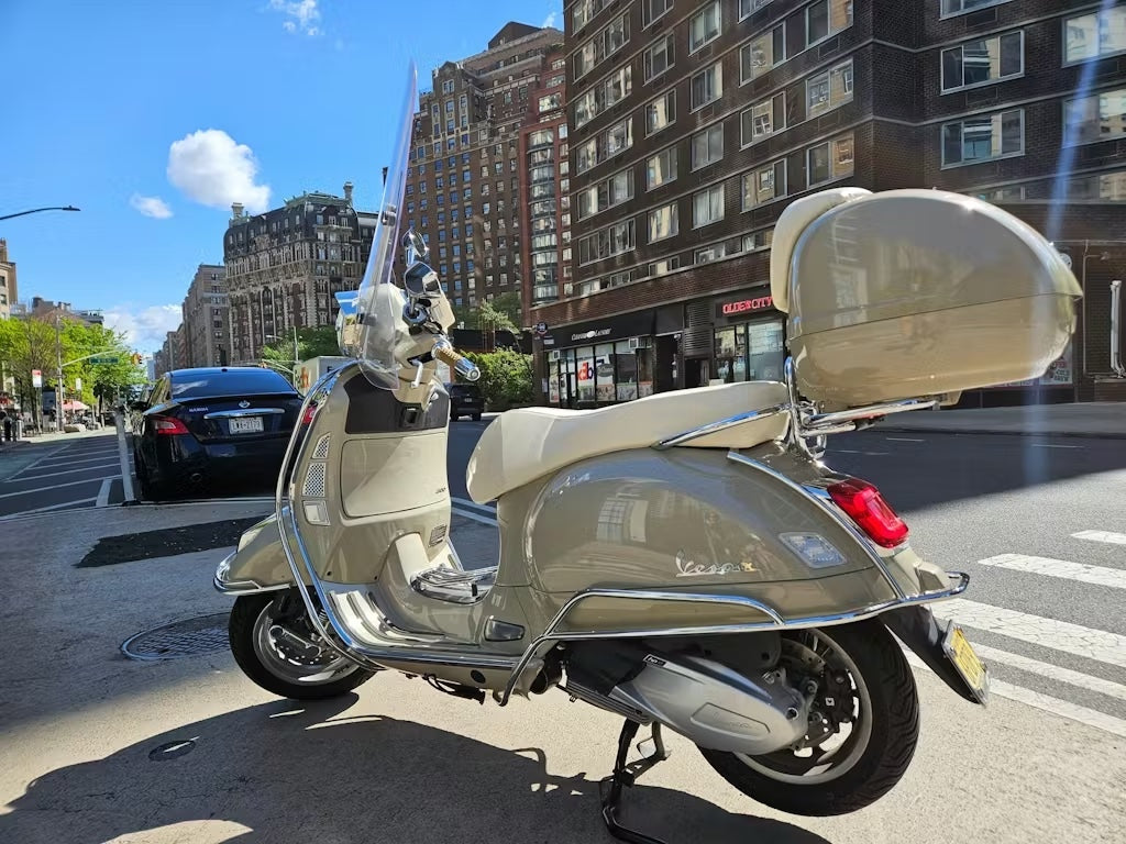 Tan Vespa GTS 310 parked on a city street with a cream color seat cover handmade by Cheeky Seats