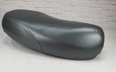 Low side view of a gray carbon-fiber-textured Yamaha Zuma II BWS 49/50 Prebug seat cover, handmade by Cheeky Seats