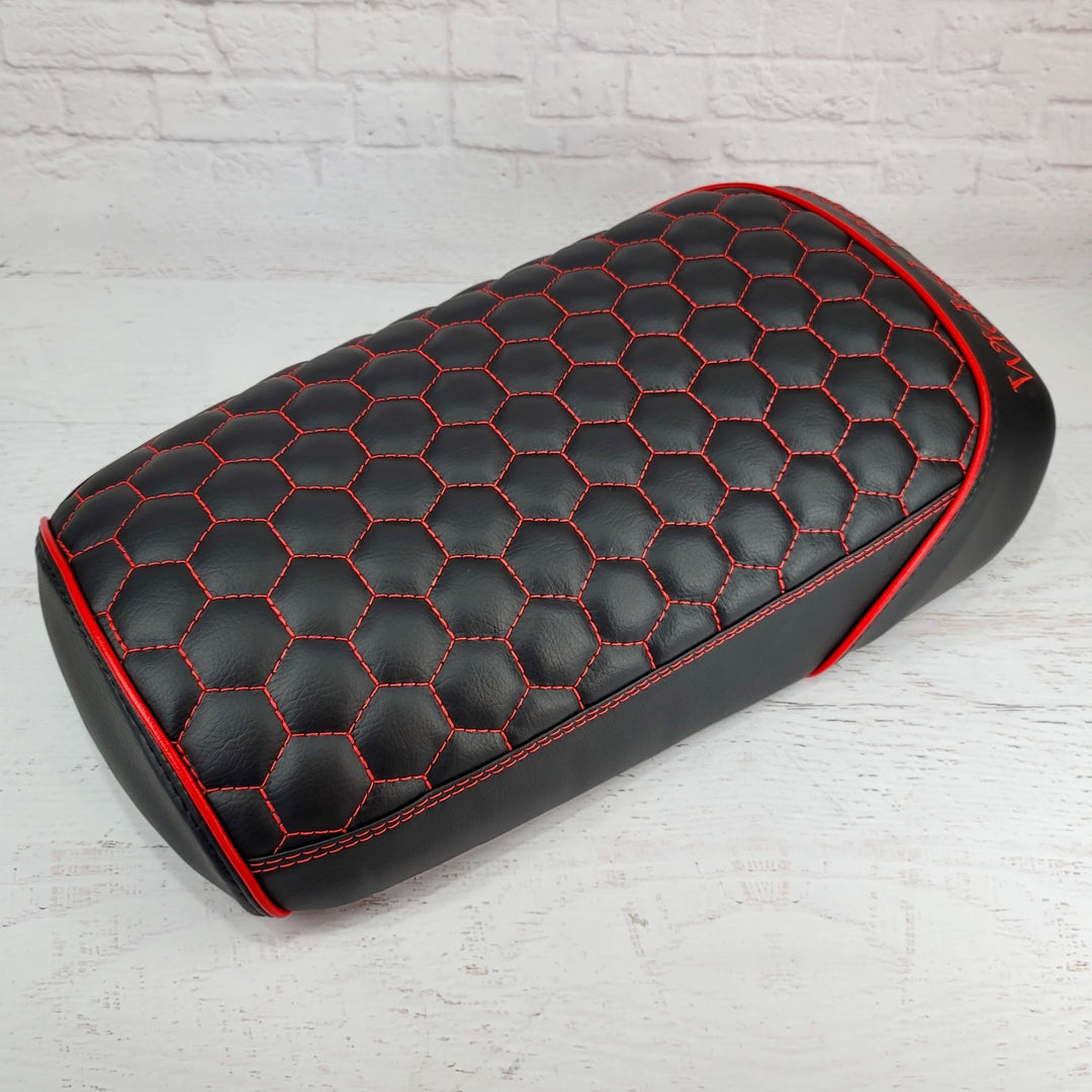Black hexagon honeycomb-stitched Maddog seat cover with red stitching and red piping, three-quarter view against a white brick backdrop, handmade by Cheeky Seats
